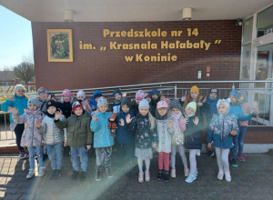 Dzieci stoją pod budynkiem przedszkola, jedno z dzieci trzyma w ręku maskotkę Krasnala Hałabały.